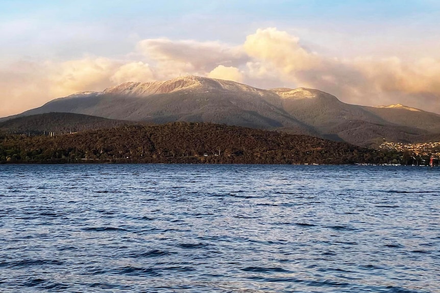 A snowy mountain with water in the foreground.