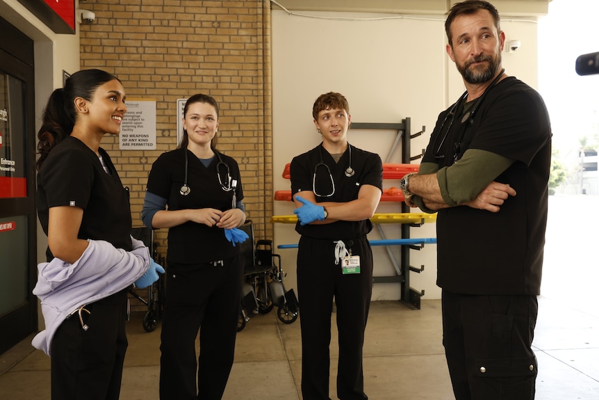 A TV still of Noah Wyle, 54, in scrubs, standing outside an ER, with Shabana Azeez, Isa Briones and Gerran Howell.