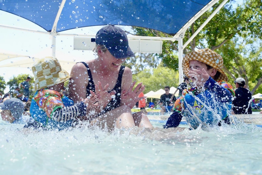 A woman and her two children play in the water.