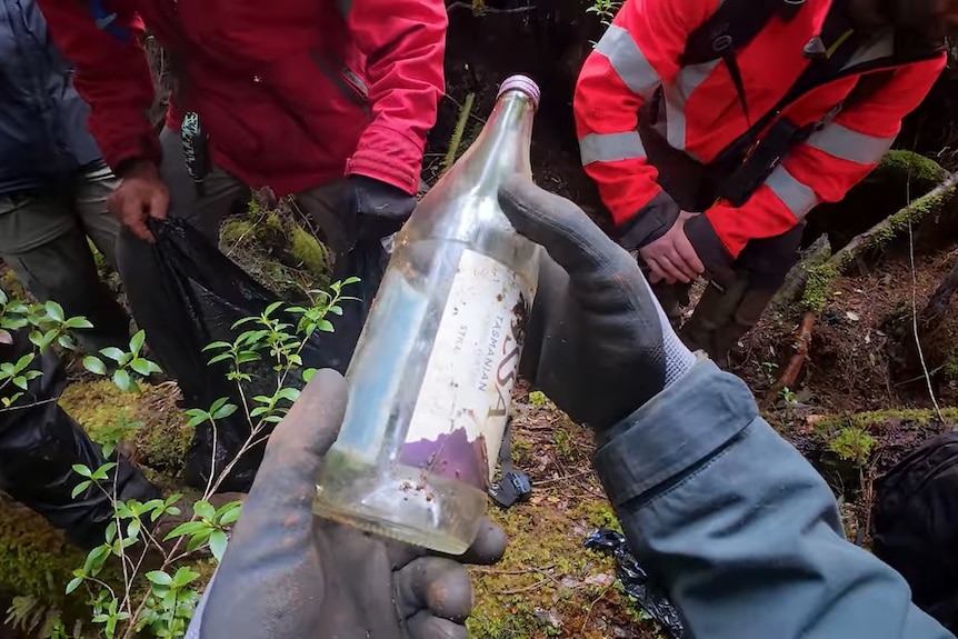A group of unidentified people looking at a glass bottle.