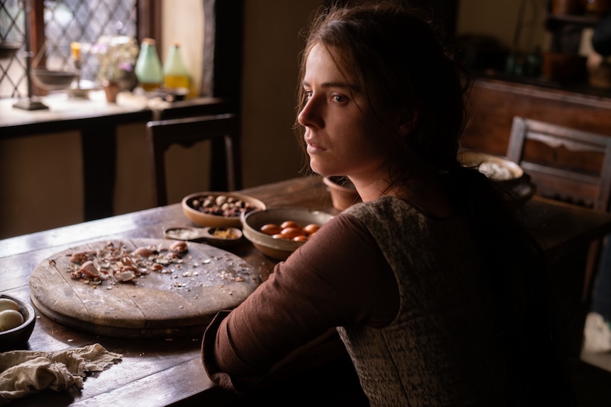 A woman sits at a table full of debris