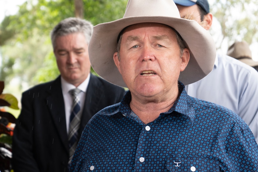 Man standing with a hat standing up and talking. 