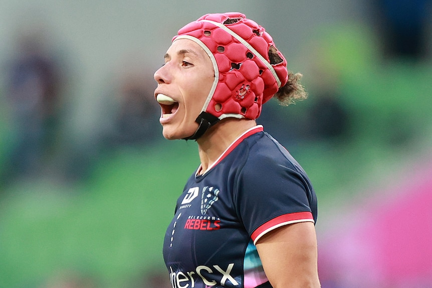 Female rugby union player Melanie Kawa is on the field shouting instructions, wearing pink headgear and a mouthguard