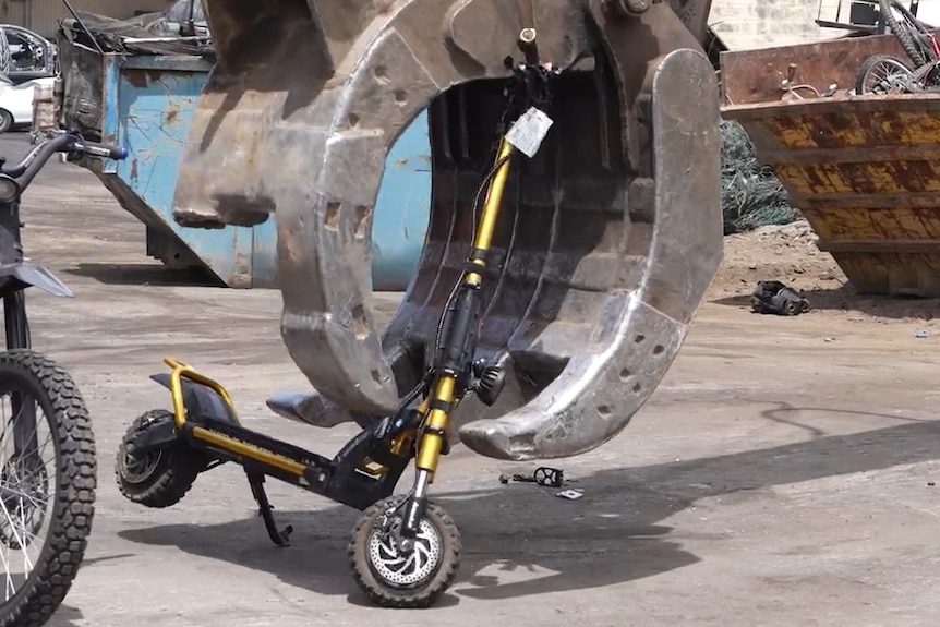 A scooter being picked up by a big metal machinery claw.