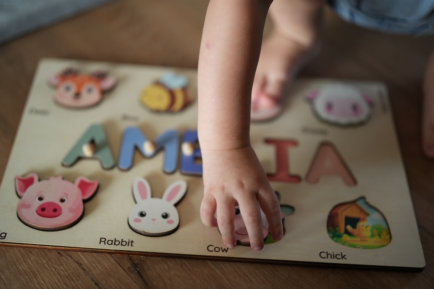 A small baby's hand on a puzzle that spells out Amelia.