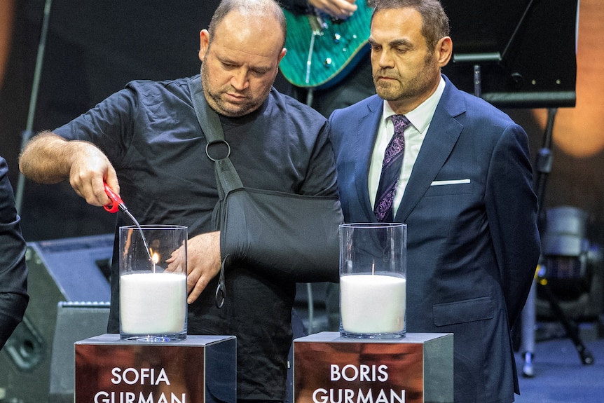 Ahmed al Ahmed (left) lighting a candle with one hand and his other arm in a sling.