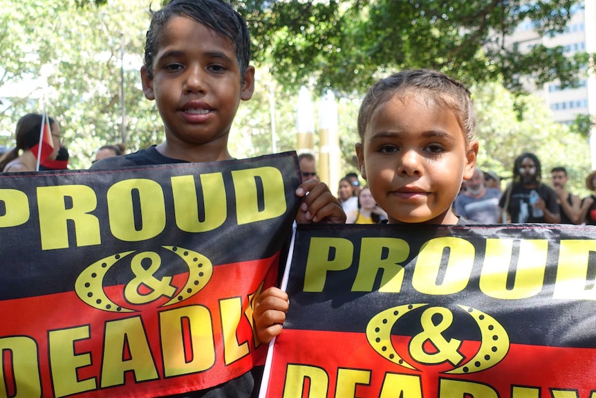 Two children holding Aboriginal flags that read "proud and deadly".