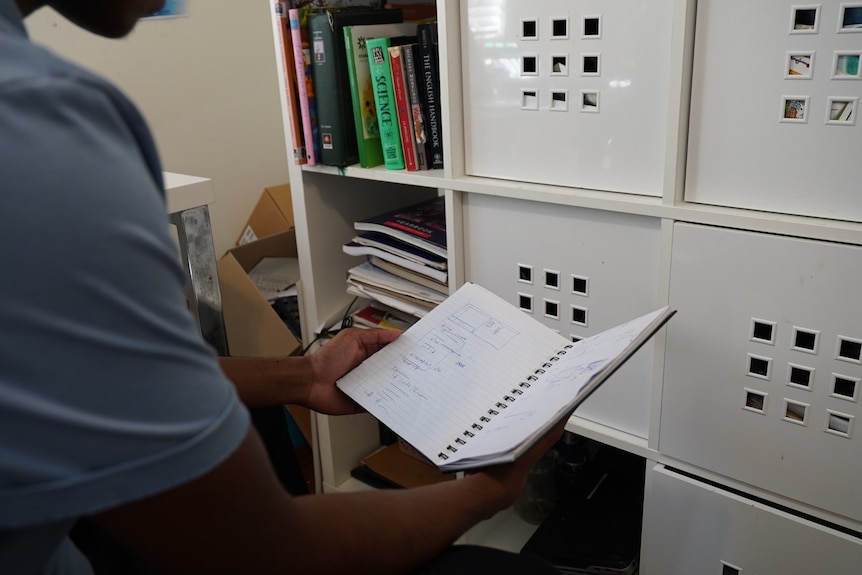 A teenager holds open a note book with coding notes written inside.