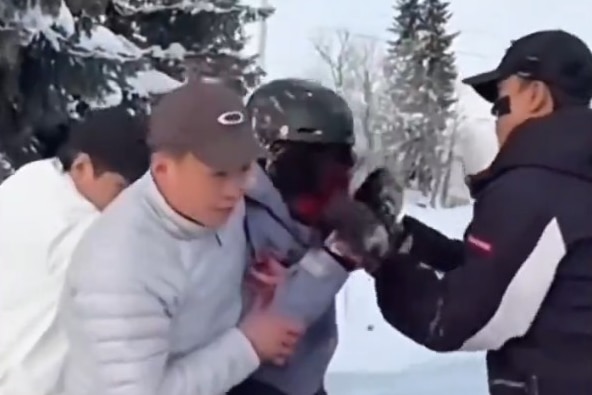 A woman in ski gear is helped thorugh the snow while she cluthces her face 