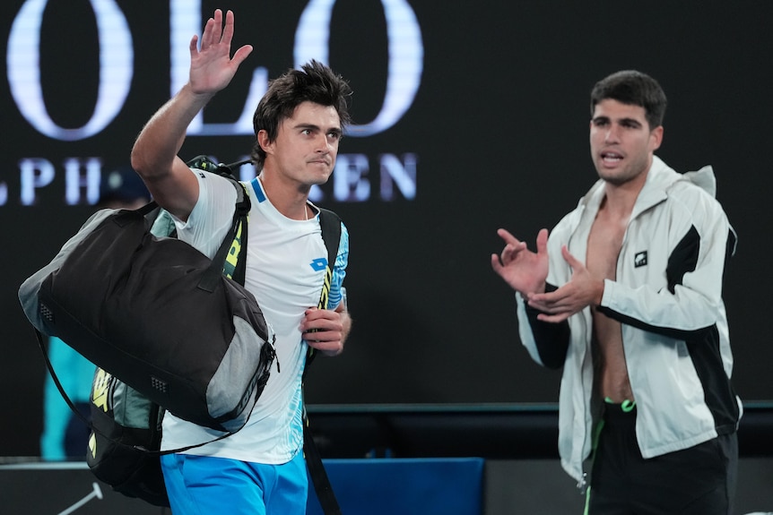 Adam Walton waves to the Rod Laver Arena crowd as Carlos Alcaraz waves in the background.