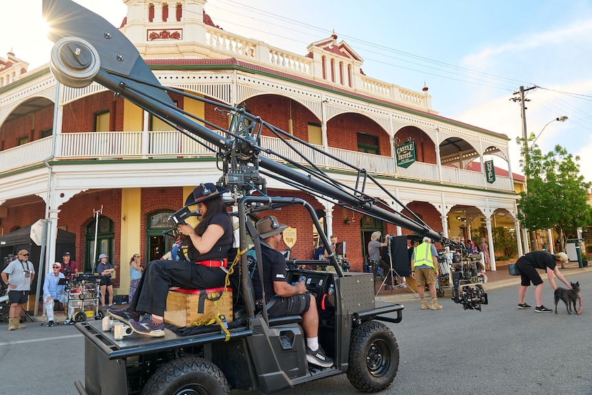 A golf cart with a camera and filming equipment drives down a road.