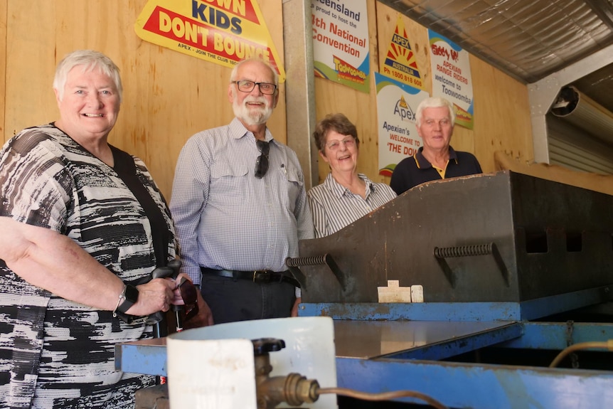 Four people stand in front of a barbecue.