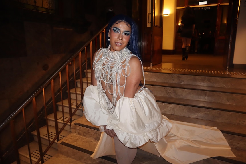 A person looking glamorous wearing a white costume with full make-up on and pearls around their neck.