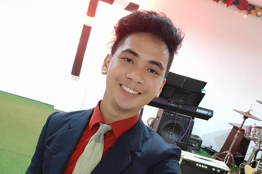 A young, dark-haired man in a suit stands near a stage with music equipment on it.