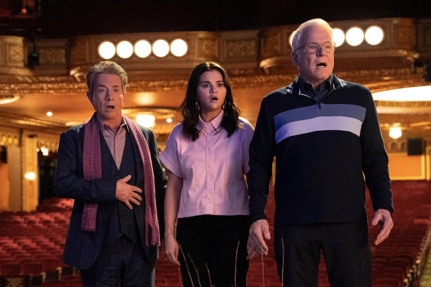 Martin, Selena and Steve look at something beyond the camera with a shocked expression as they stand on a stage.