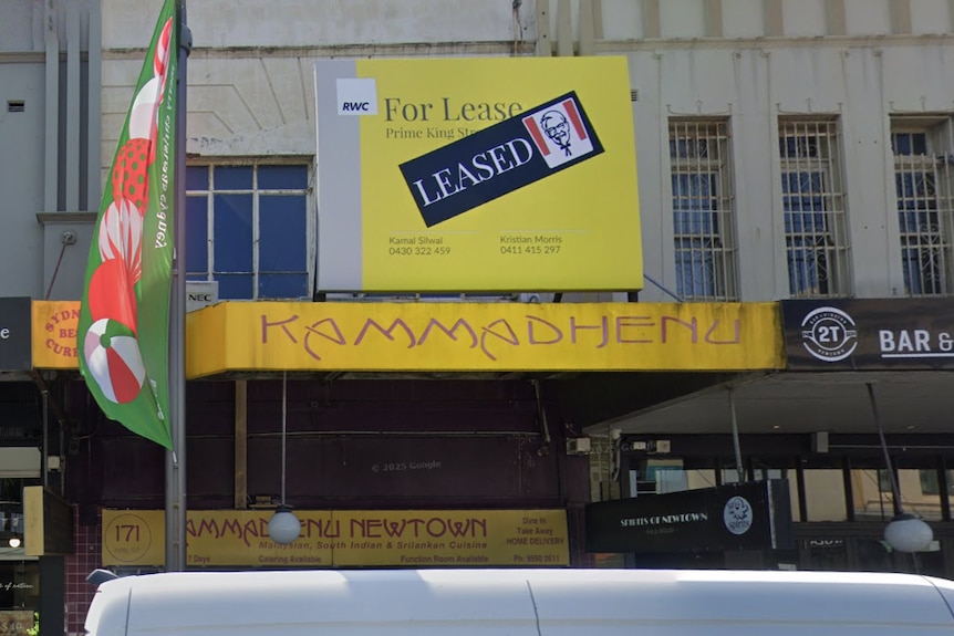A 'for lease' sign above the Kammadhenu restaurant with a sticker over it saying 'leased' next to a KFC logo.
