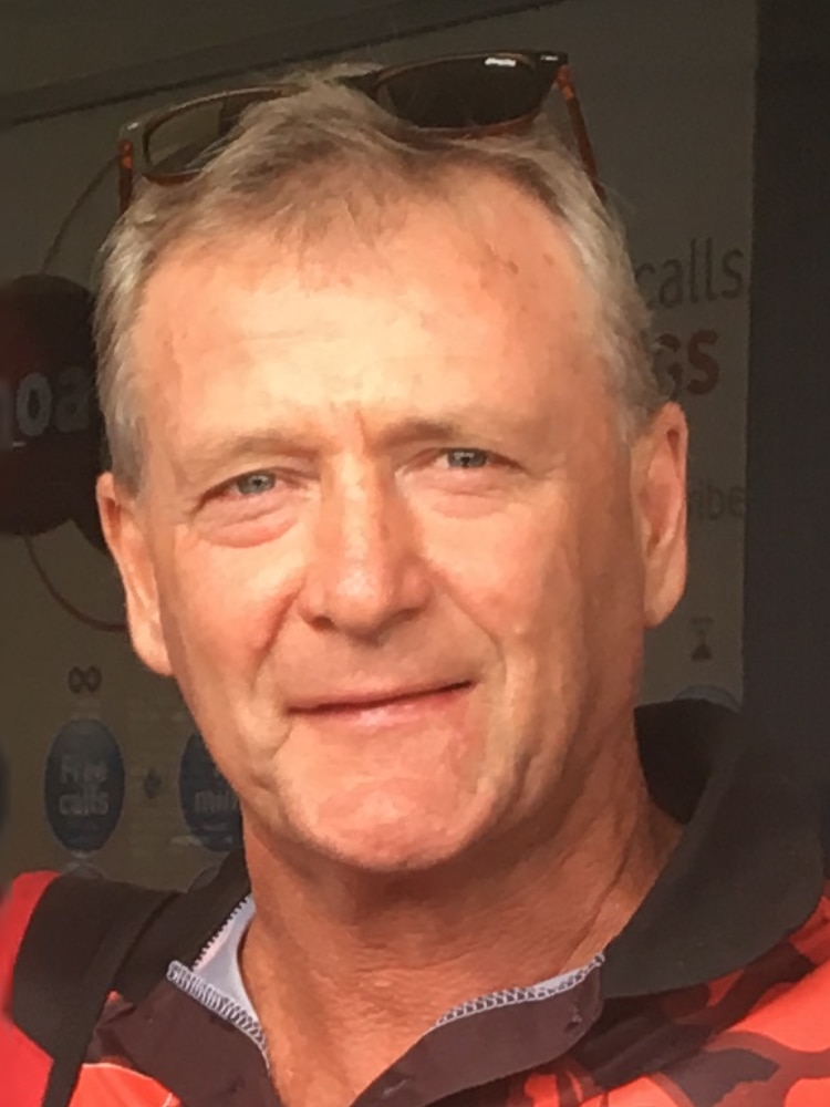 Headshot of a man wearing an orange and black polo shirt. He has short hair.