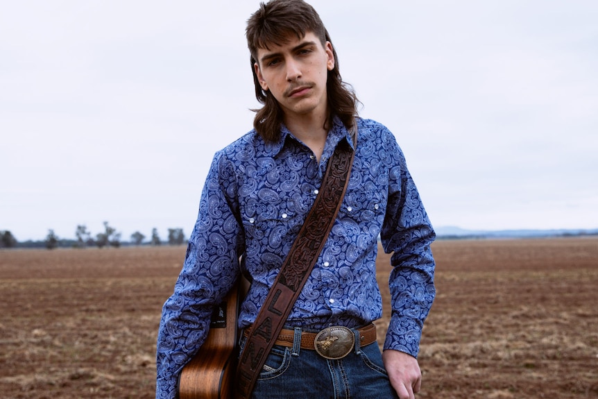 A man in a field with a guitar hanging across his body .
