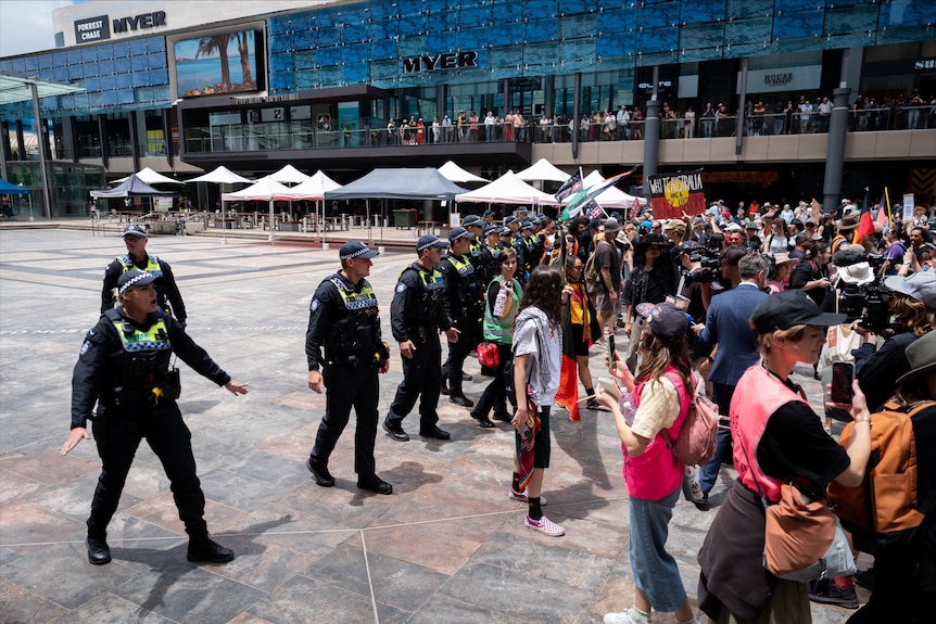 A row of police push back a crowd in Perth's CBD