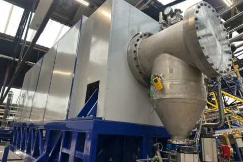 A large machine - mainly grey, but also blue near the bottom - inside a building.