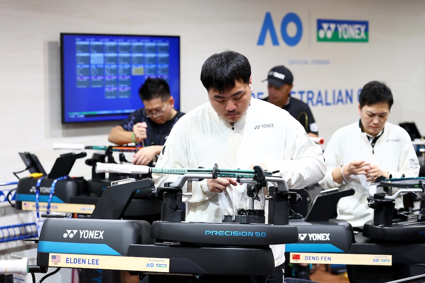 A man looks down while touching a tennis racquet