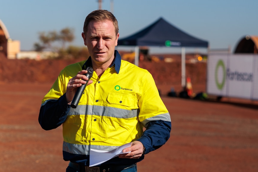 A man wearing high vis holding a microphone, addressing a crowd at a Fortescue event