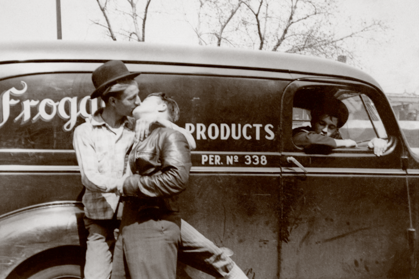 Two men kissing in front of a car.