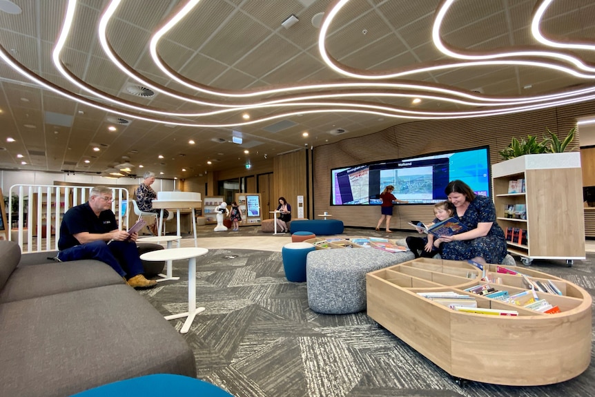 People sitting in a library filled with book bins, desks and sofas