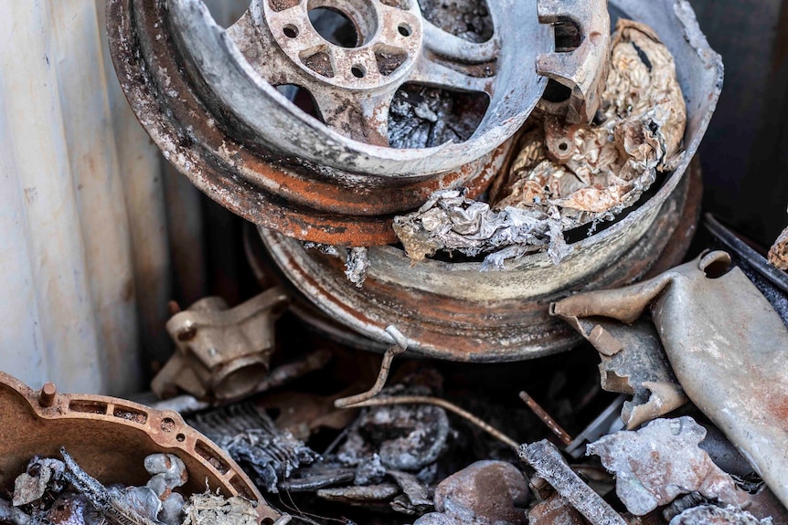 Metal hubcaps and other metal items items are piled against a corrugated iron wall.