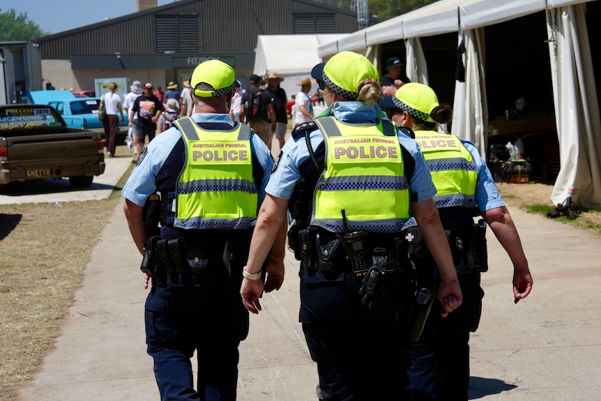 Three police officers patrol a car festival.