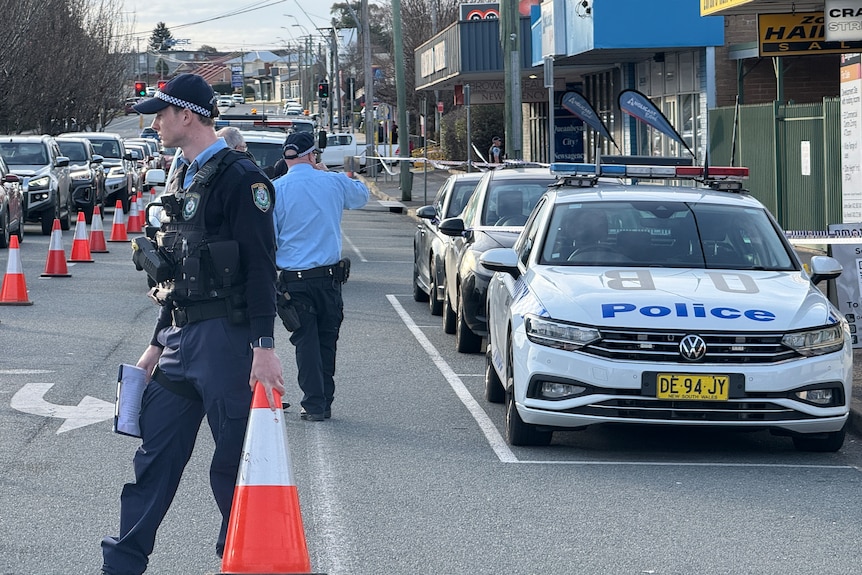 Three uniformed police officers walking on a road blocked off with orange cones.