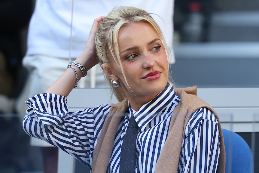 A young blonde woman wearing a striped shirt and tie looks to the side while smiling at the Aus Open.