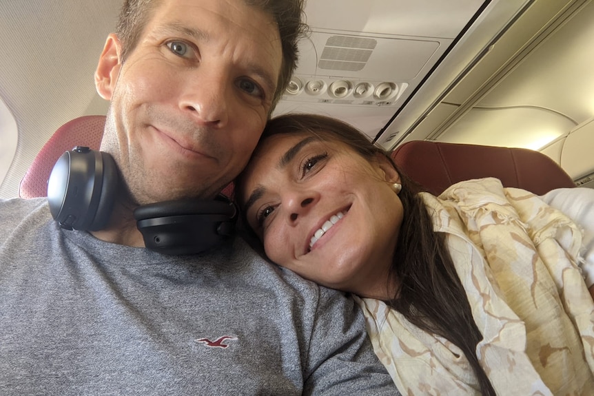 A man and a woman taking a selfie on a plane, with her head resting on his shoulder