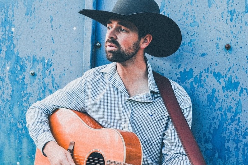 man with a guitar wearing a black cowboy hat and chambray shirt