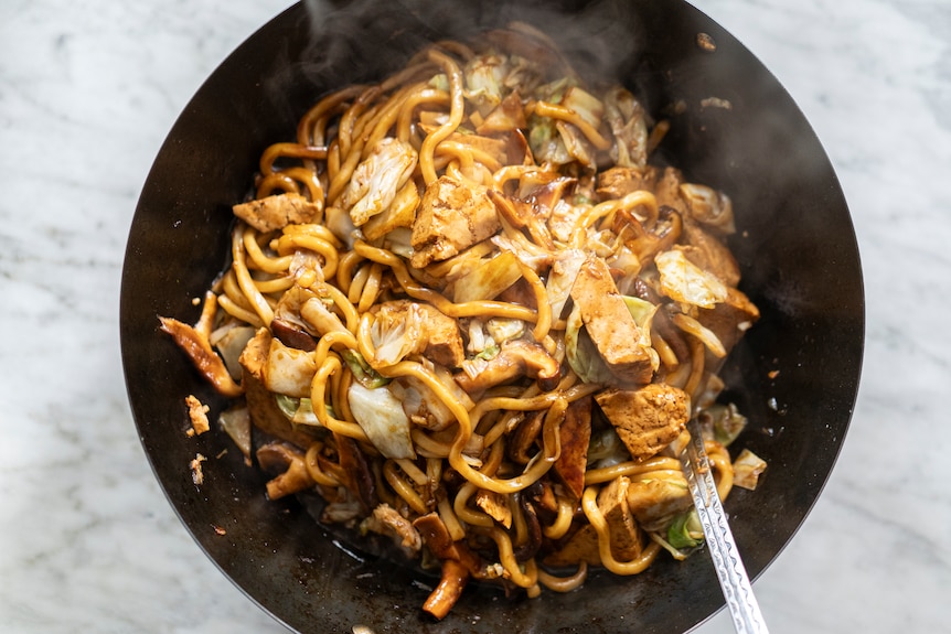 A wok of just-cooked vegan Hokkien mee. Hokkien noodles with green cabbage, shiitake mushrooms, tofu and a thick dark and swe