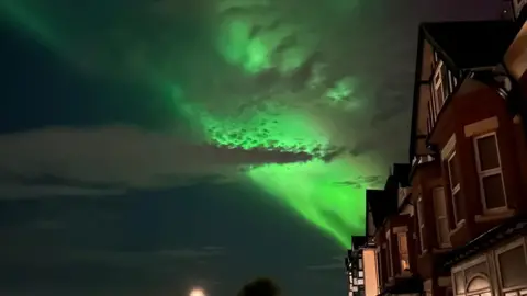 Paul Smith A view of the night sky illuminated green above a row of terraced houses