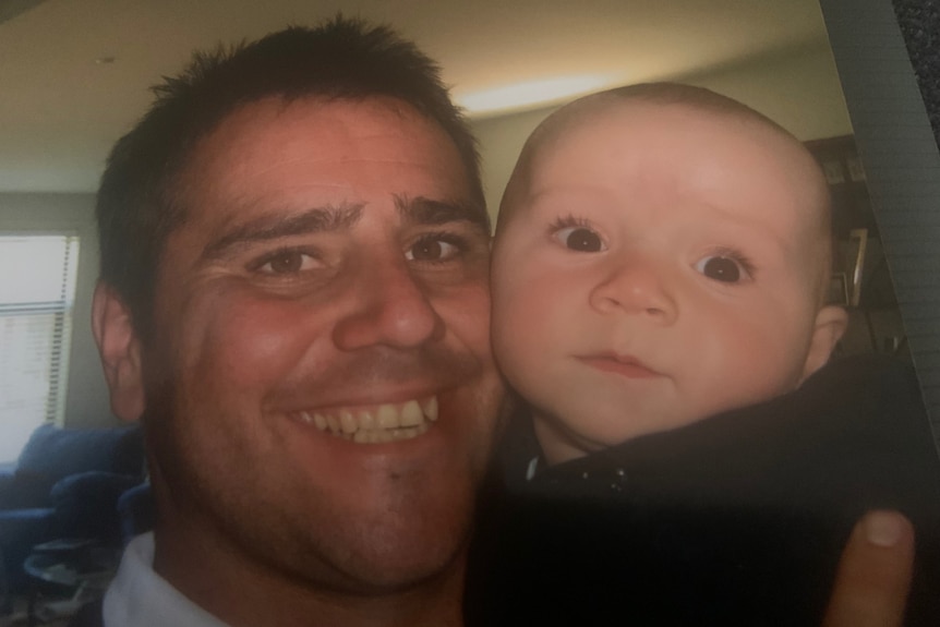 A man smiles while holding a baby.