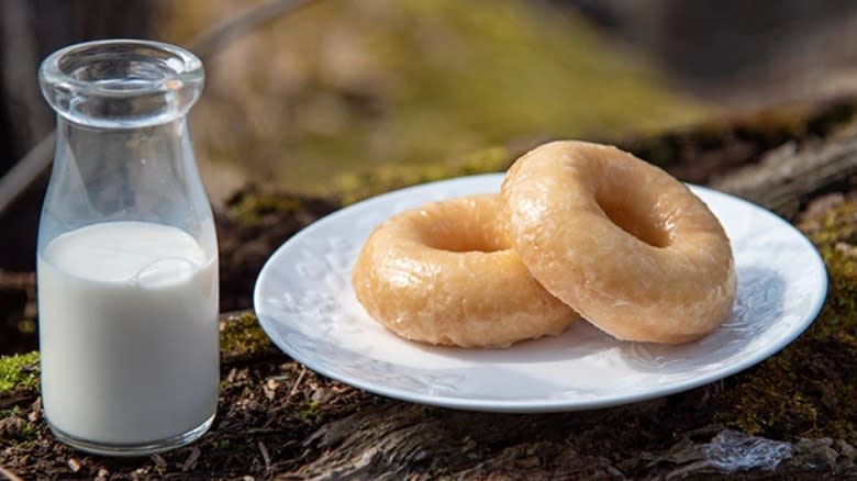 Plate with two glazed donuts and glass of milk on log