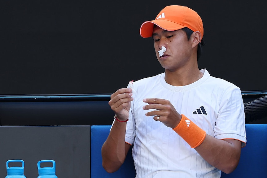 Learner Tien looks down at a tissue with blood on it, while another tissue is up his nose