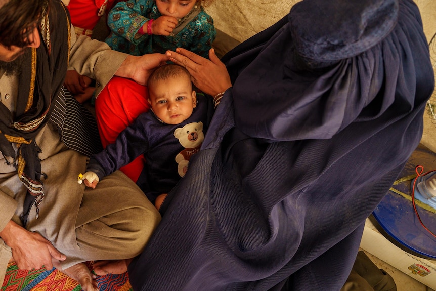A mother dressed in a burqa sits with her husband, baby and children in a tent.