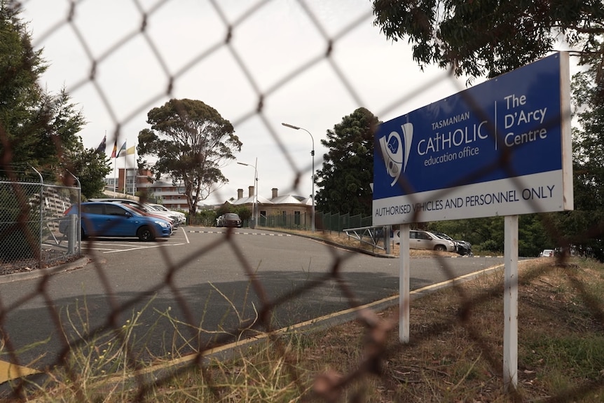 A blue sign for the Tasmanian Catholic Education Office, behind a chain link fence.