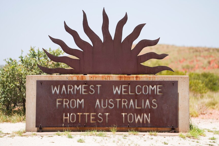 A rusted metal sign in the shape of a sun - a welcome sign to a town