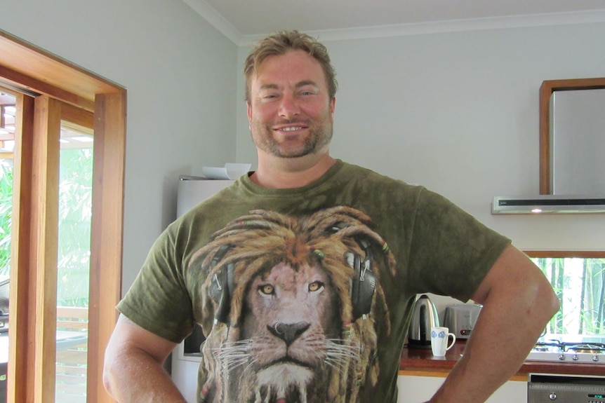 A young man smiles for the camera. He is wearing a green t-shirt with a large lion pictured on the front of it.