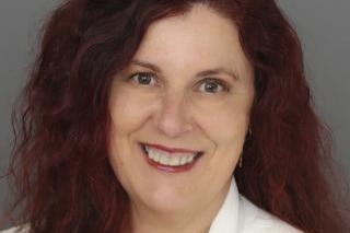 A woman with long red hair and brown eyes smiles at the camera.