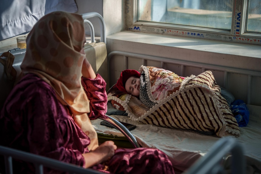 A mother sits by her sleeping baby in hospital.