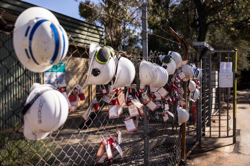 Hard hats and ID tags left on a fence by workers at the entrance to a smelter which has been closed.  