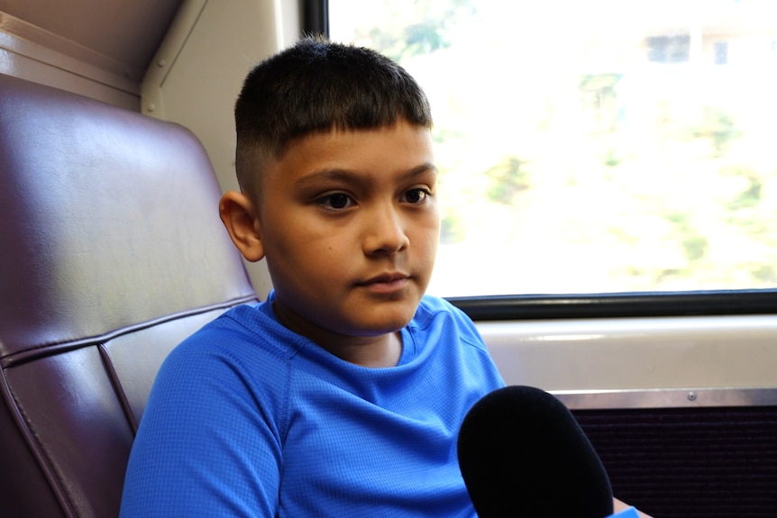 A young boy in a blue t-shirt speaks to a reporter behind the camera.