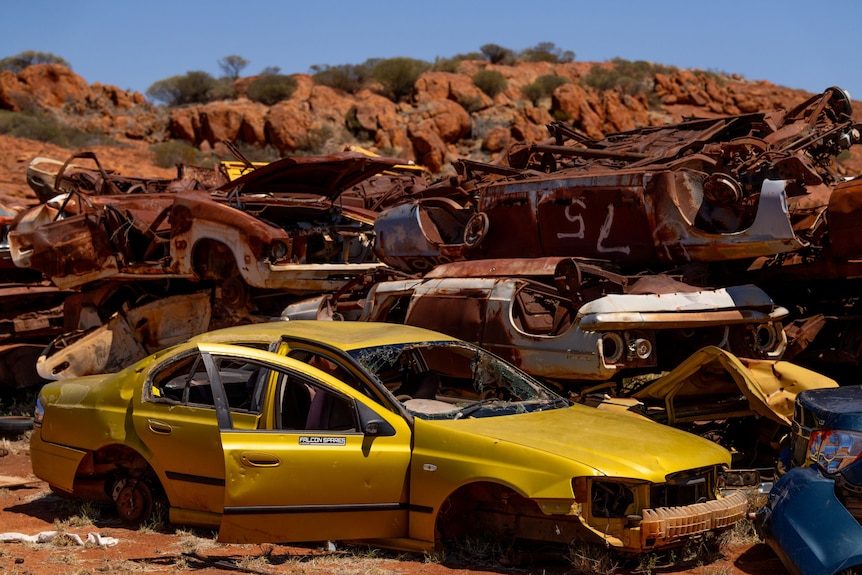 Yellow car wreck among rusty coloured cars piled up at the dump. 