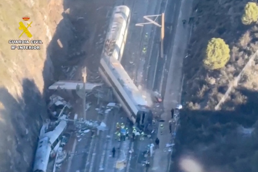 Multiple train carriages and debris strewn over a dual-track rail line in a cutting.