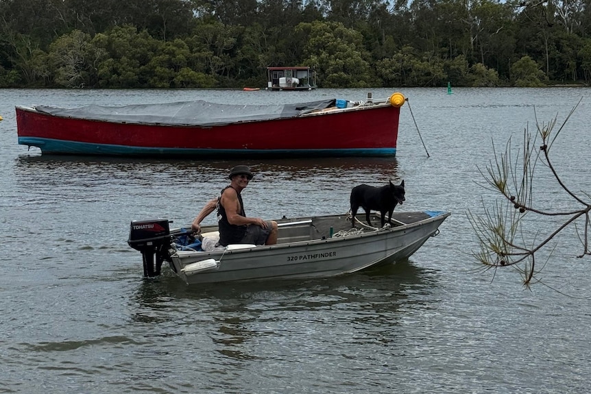 Man with dog in tinnie on river.